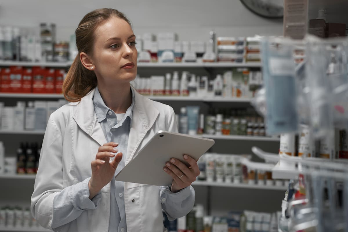 Fornecedores de medicamentos: uma mulher com jaleco andando por prateleiras de medicamentos.