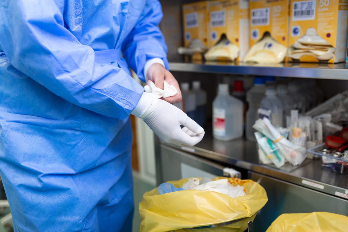 Profissional de saúde com luvas descartáveis separa materiais para descarte de medicamentos em saco hospitalar amarelo.