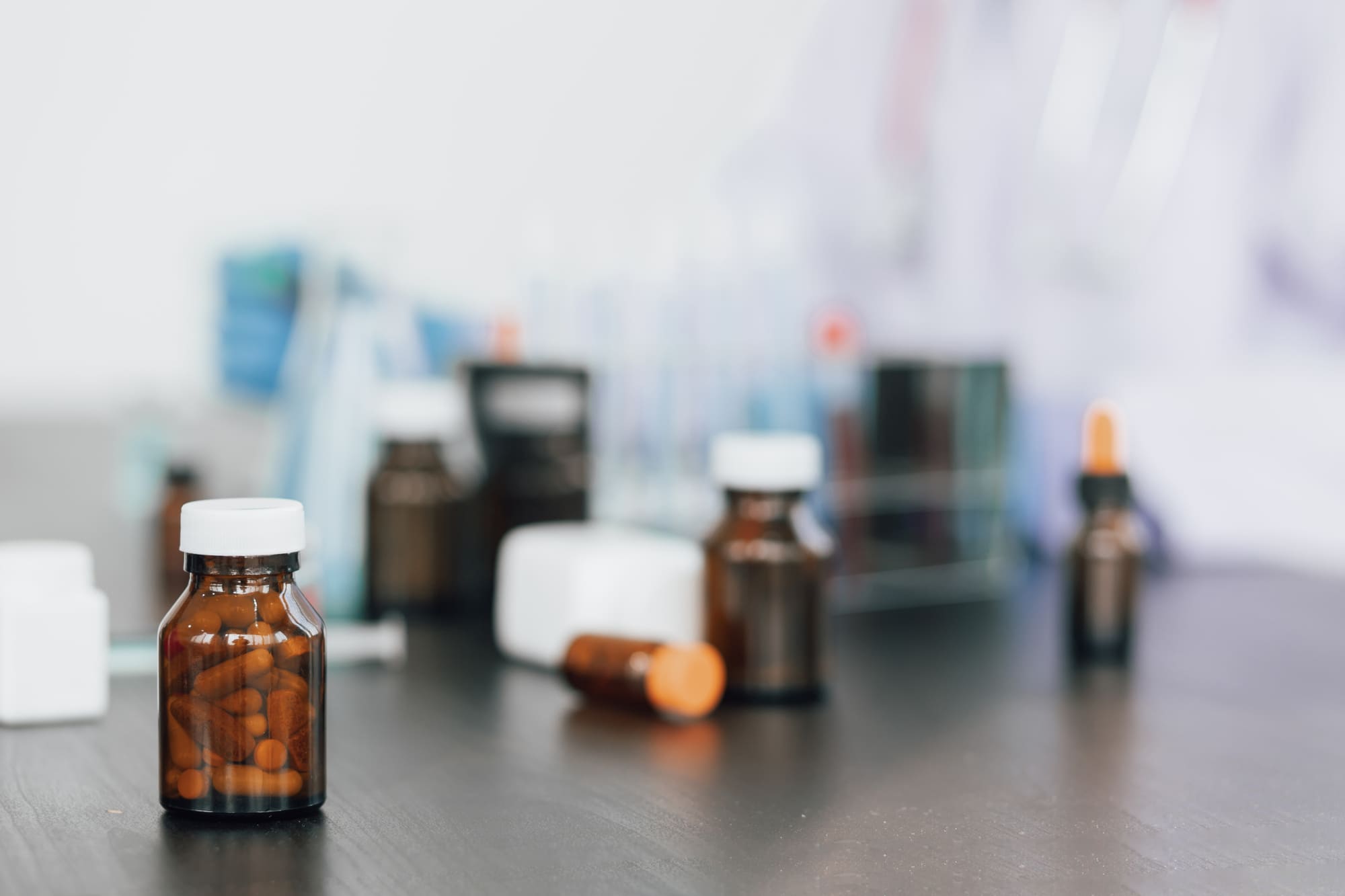 Frascos de medicamentos em vidro âmbar sobre mesa de laboratório, com cápsulas visíveis no interior.